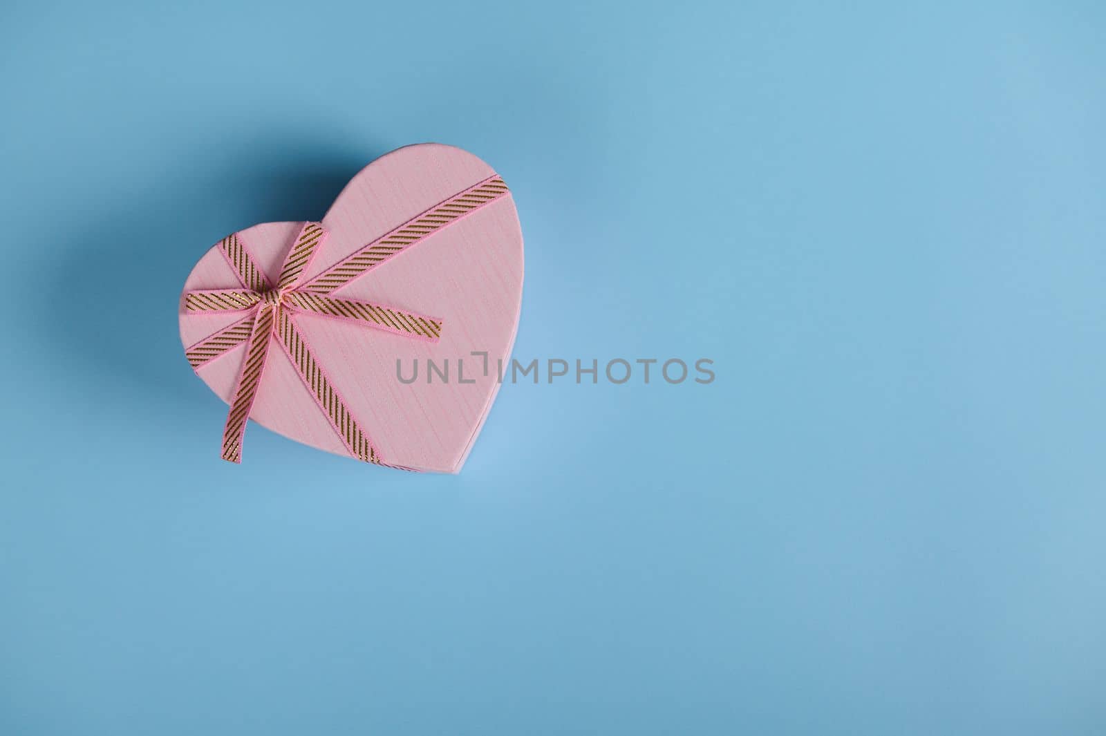 Top view Saint Valentine's day or International Women's Day heart shaped gift box, with pink ribbon bow, on pastel blue background with copy advertising space. March 8. February 14. Anniversary gift