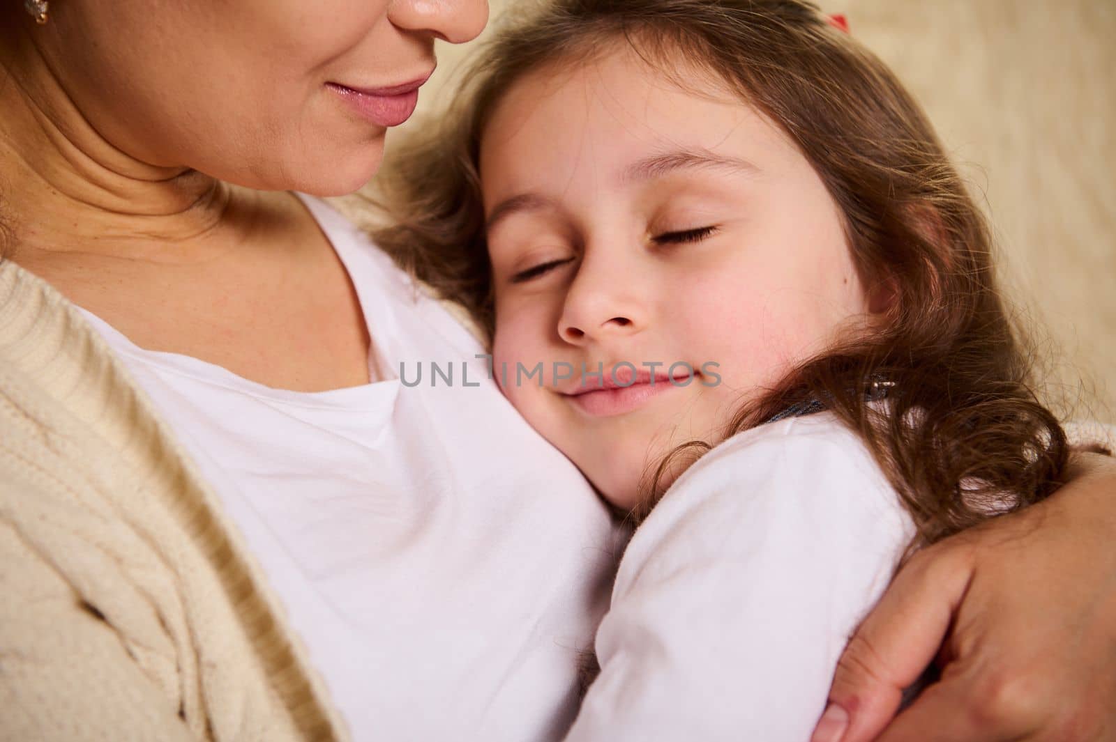 Adorable Caucasian little girl, a beautiful calm beloved daughter falling asleep on her loving mother's hands. Love. Tenderness. Embrace. Happy carefree childhood. Close-up portrait.