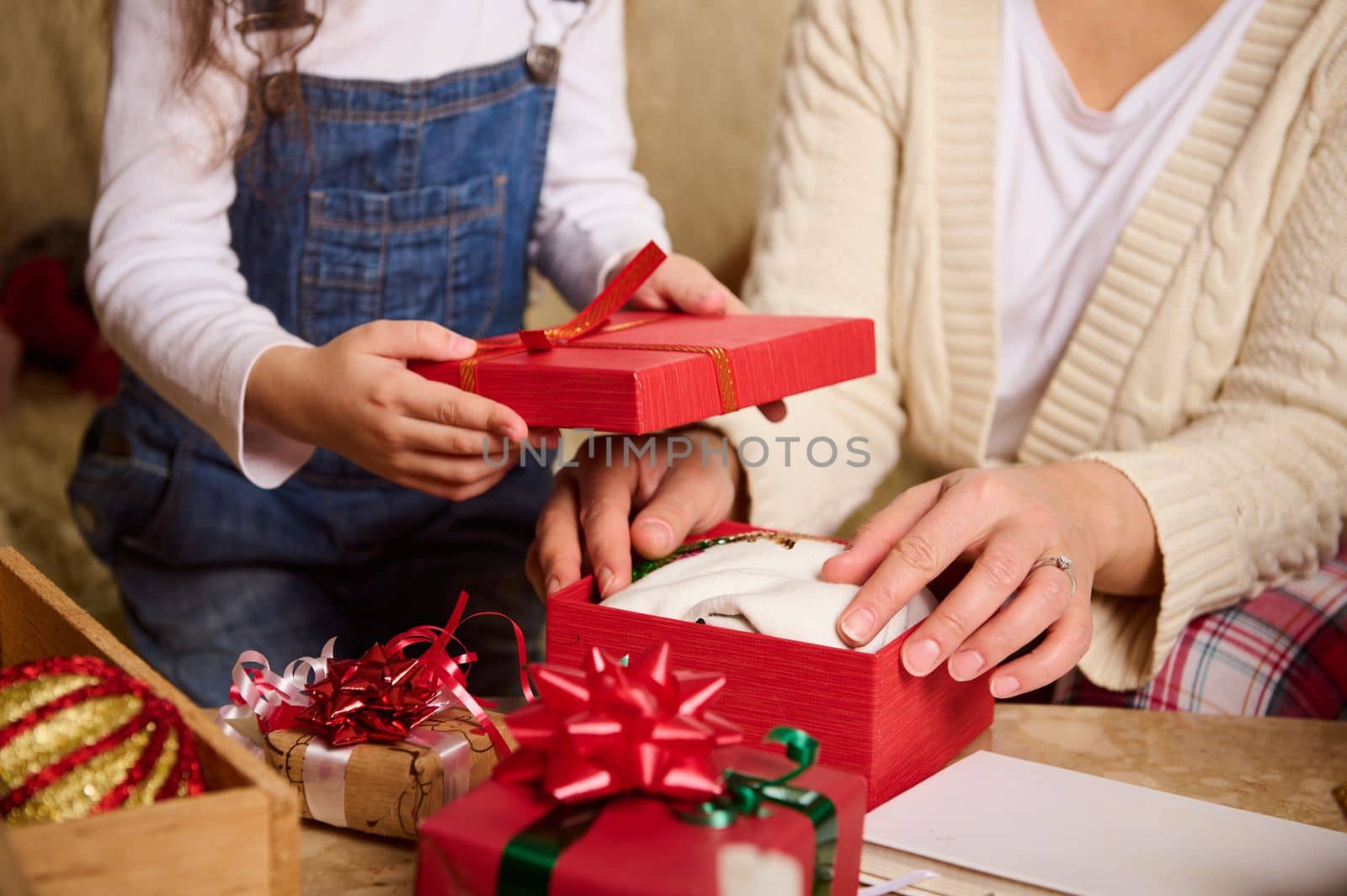 Close-up mother and daughter packing presents for Christmas or New Year, looking forward at the upcoming winter holidays. Happy family relationships. Magical festive atmosphere at cozy home interior