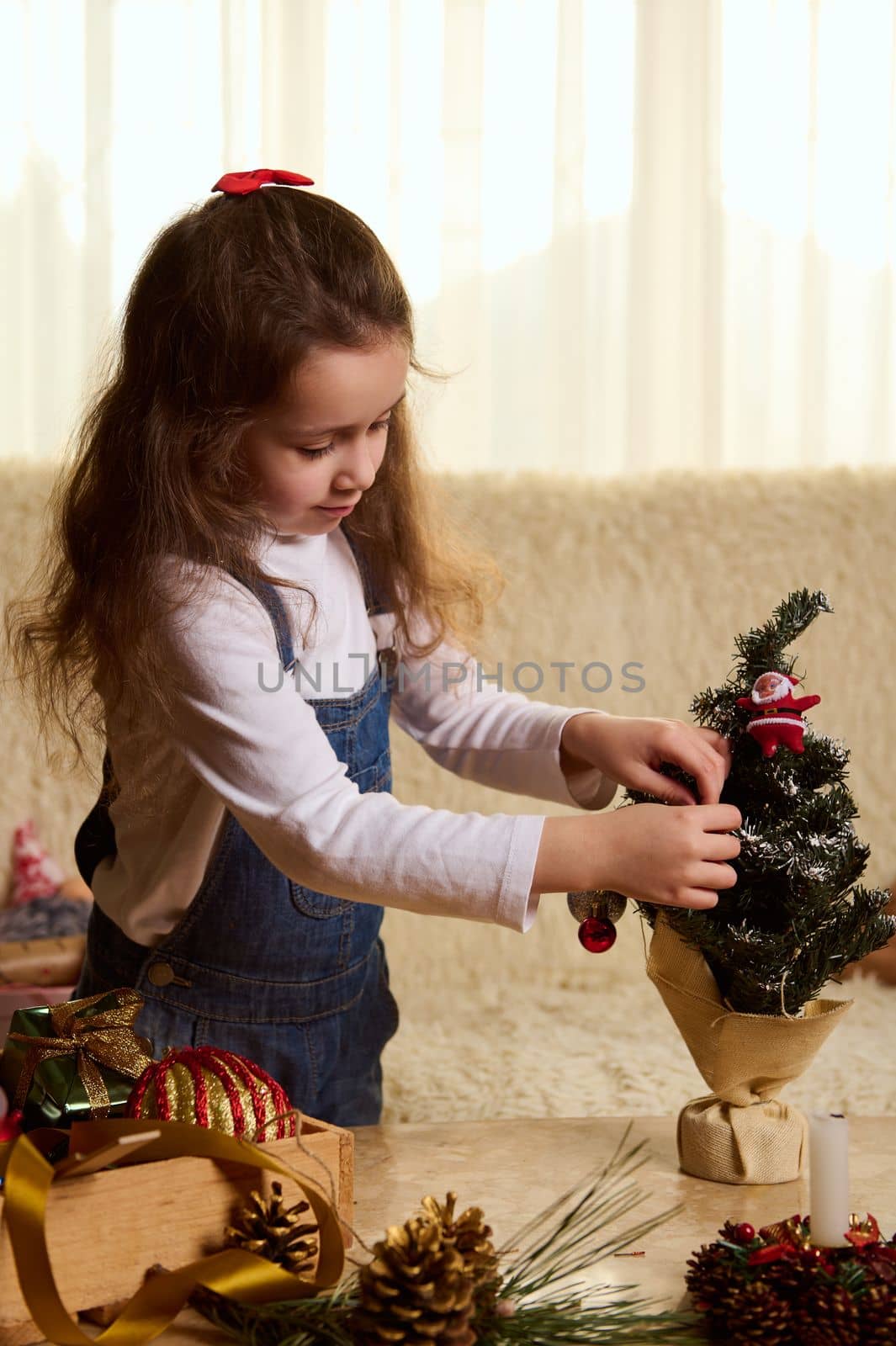 Adorable little child girl is decorating a Christmas tree with beautiful toys. New Year's preparations. Winter holidays by artgf