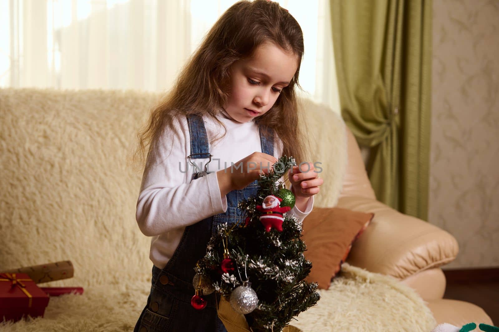 Beautiful little girl hanging decorative balls and ornaments on a Christmas tree by artgf