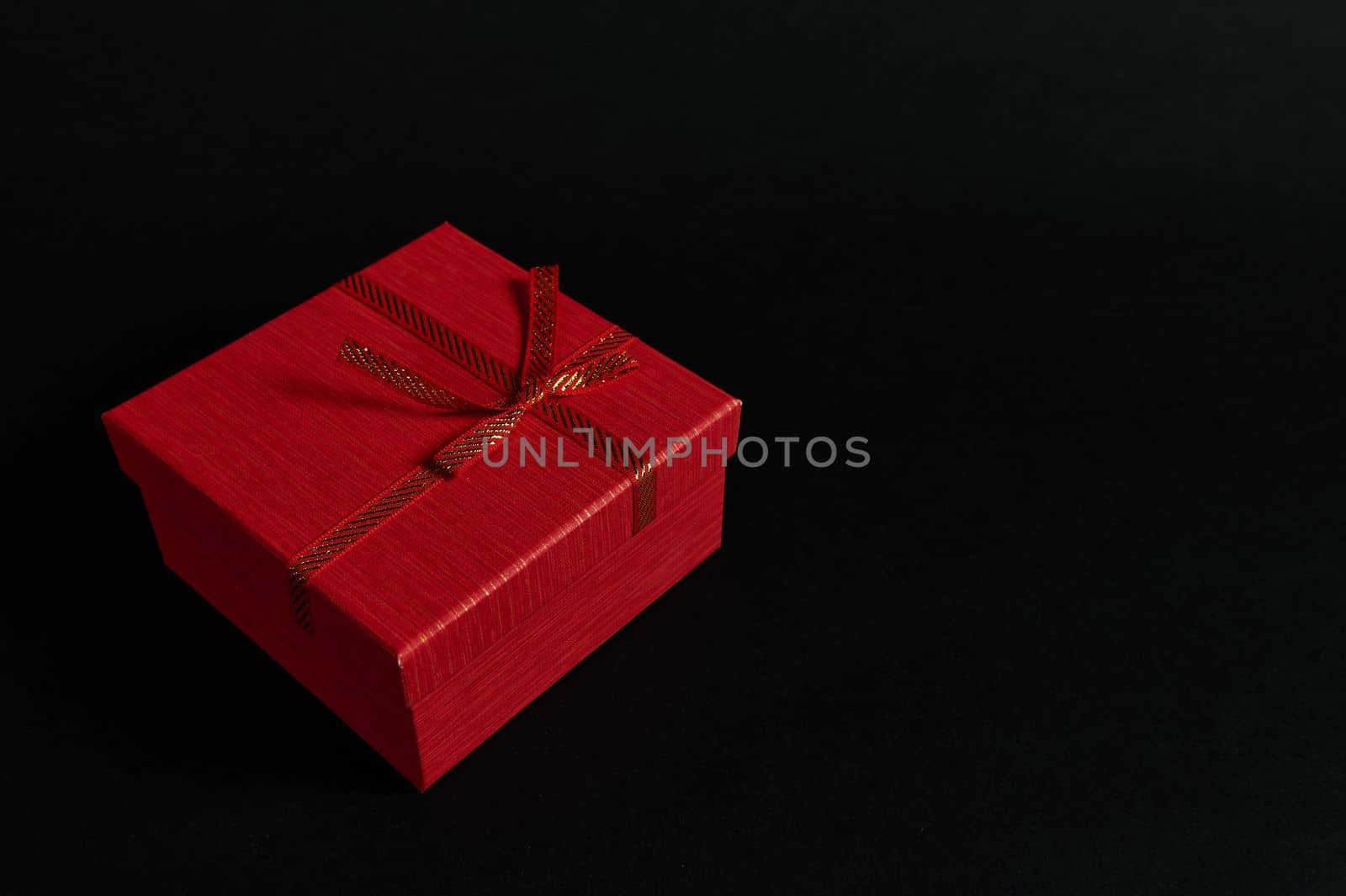 Still life red cardboard present box with a tied bow isolated on a black background with advertising copy space. Web banner. Top view of Christmas gift with surprise, packed in an elegant gift box.
