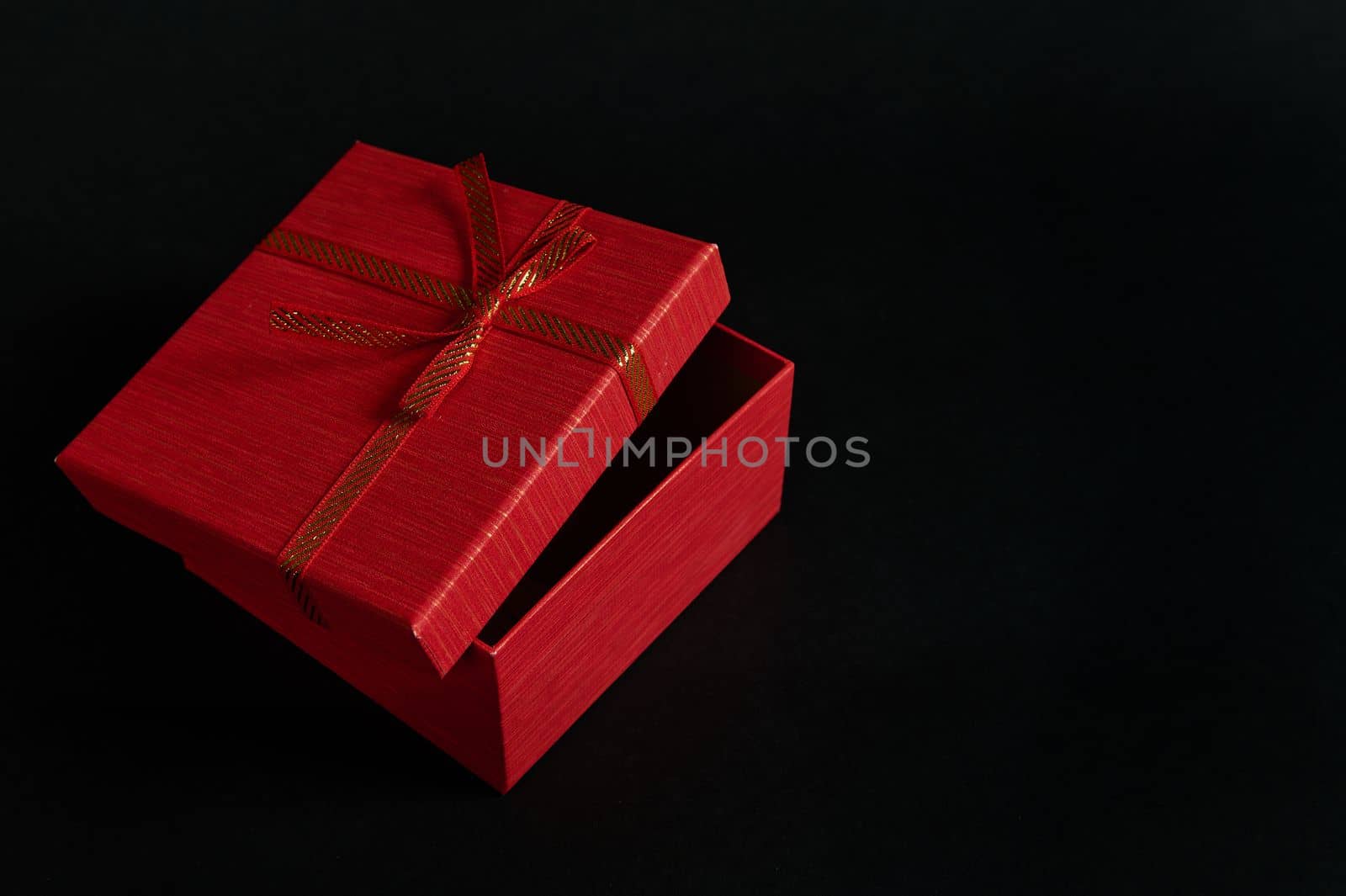 Still life red cardboard gift box with an opened lid and tied bow, isolated over black background with advertising copy space. Christmas or Valentine's Day concept. Boxing Day. Anniversary