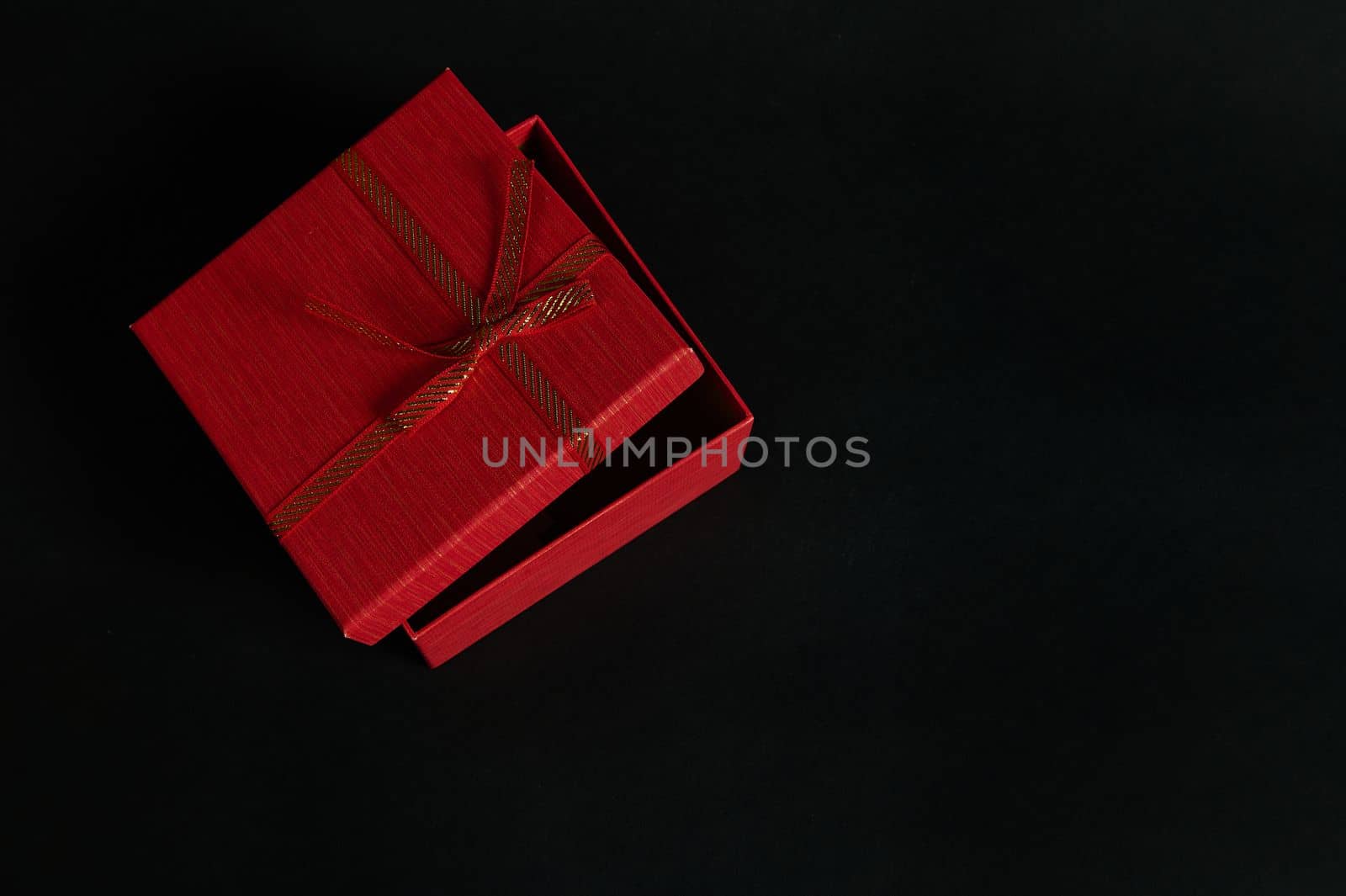 Half open elegant red cardboard gift box with a tied bow isolated on a black background with copy ad space for promotional text. Christmas gift. Valentine's Day. Women's Day. Mothers Day. Black Friday