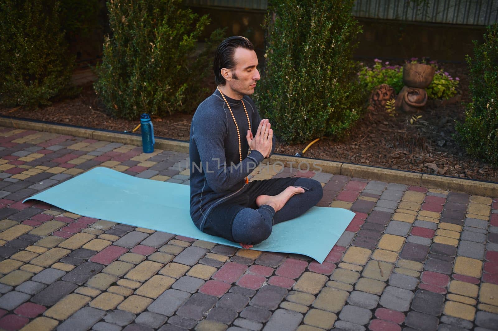 Male yogi keeping hands palms together, meditates on a fitness mat with rosary beads. Yoga practice. Mindfulness by artgf