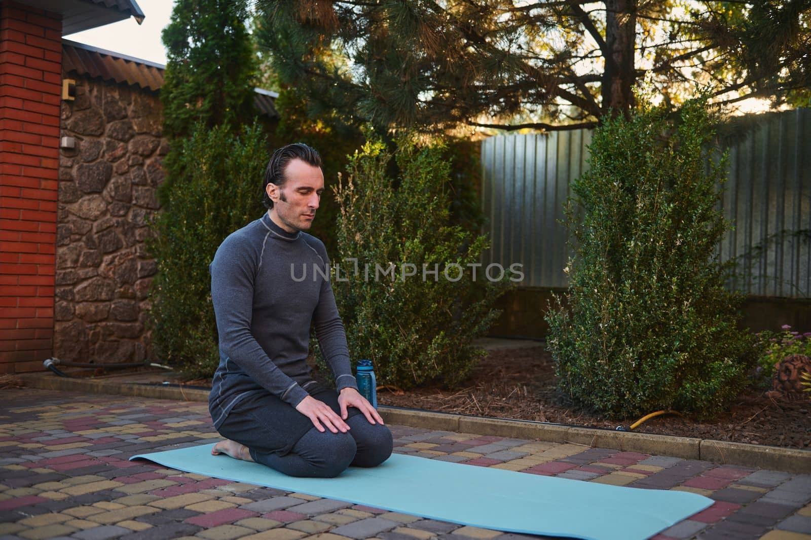Middle aged active man yogi sitting on a fitness mat, practicing breathing and relaxation exercises outdoors. Yoga by artgf