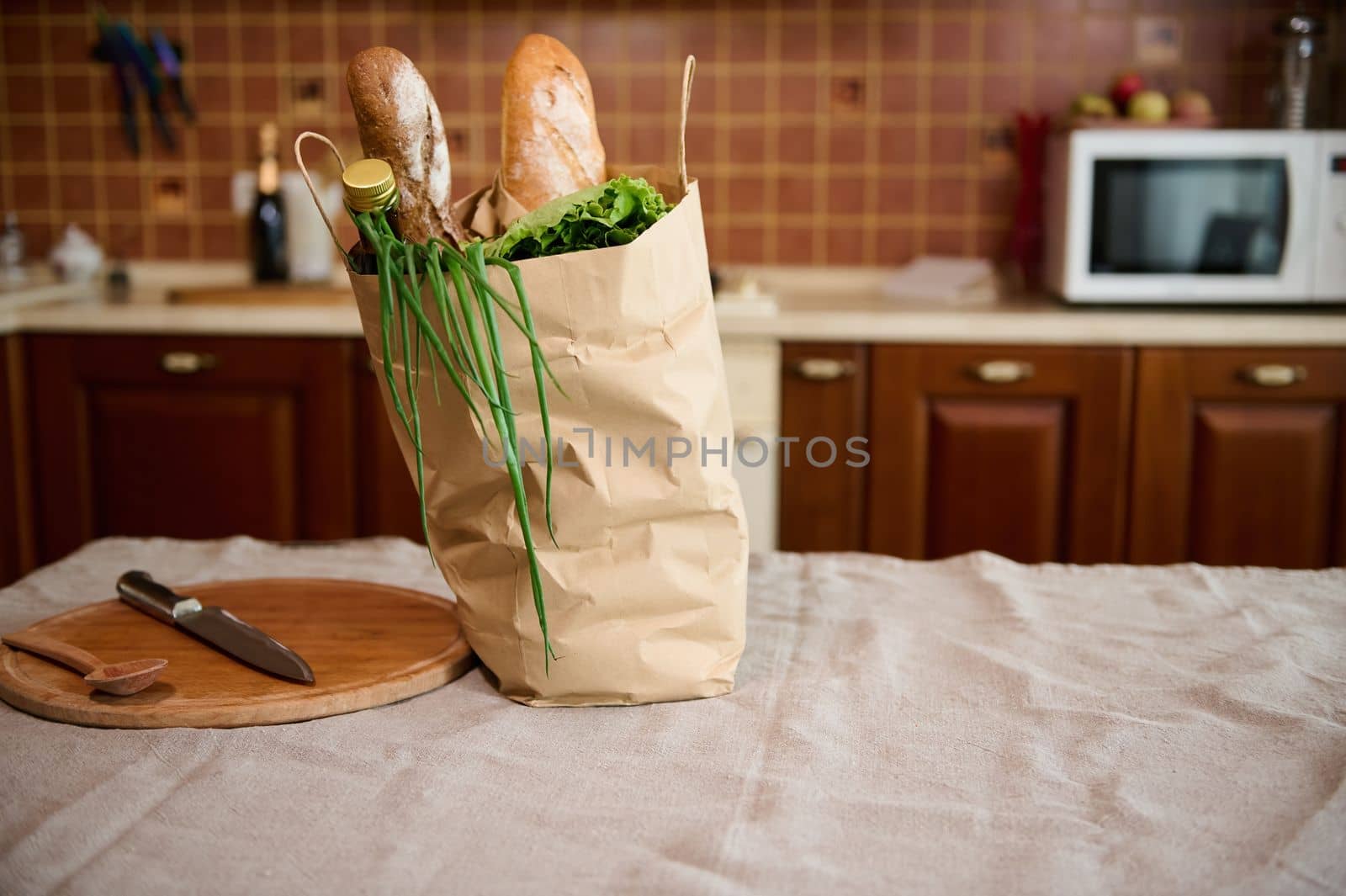 Eco paper bag with loaves of whole grain bread, greens and groceries on the kitchen island. Home delivery of farm products