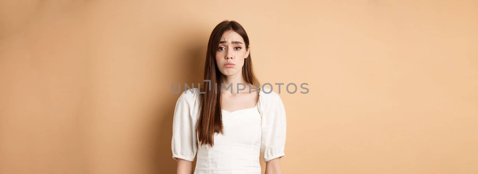 Please I want it. Silly woman make cute sad eyes and begging to buy her something, standing with innocent pleading loo, beige background by Benzoix