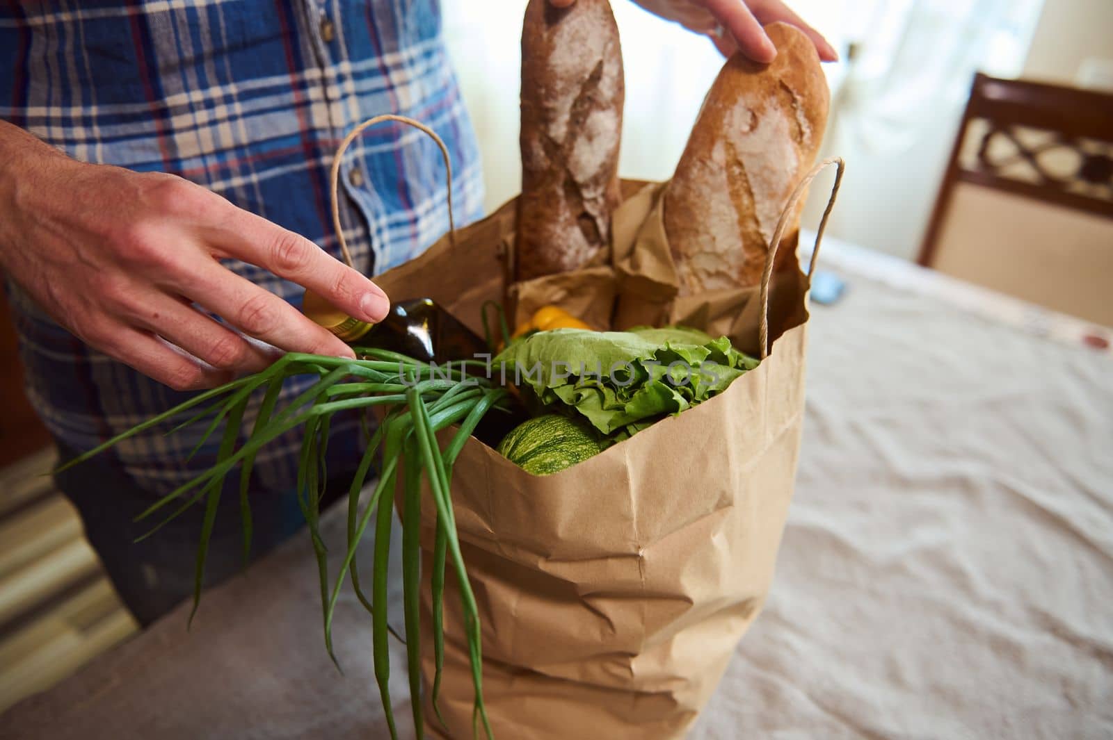 Overhead view of a guy sorting organic fresh vegetables while unpacking grocery shopping bag in the kitchen at home. Food delivery. Healthy grocery purchasing in farmers markets and stores