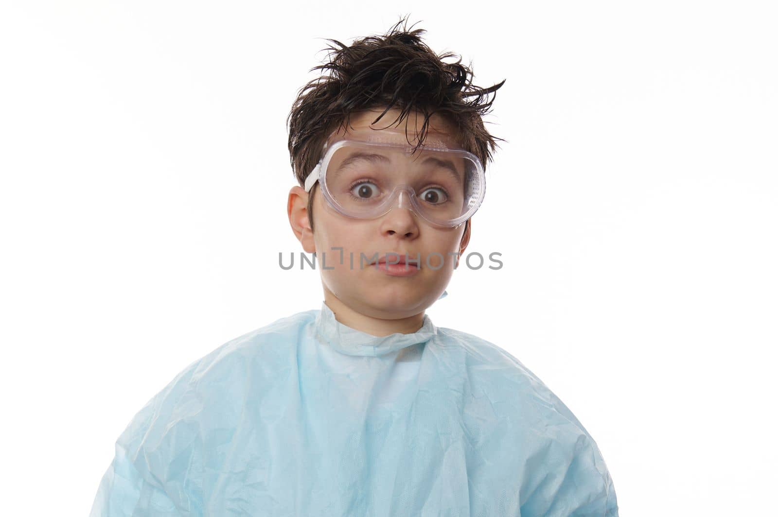 Close-up studio shot of an amazed smart teenage boy, nerd chemist scientist in labwear and goggles, looking at camera with astonishment, isolated on white background with free advertising space