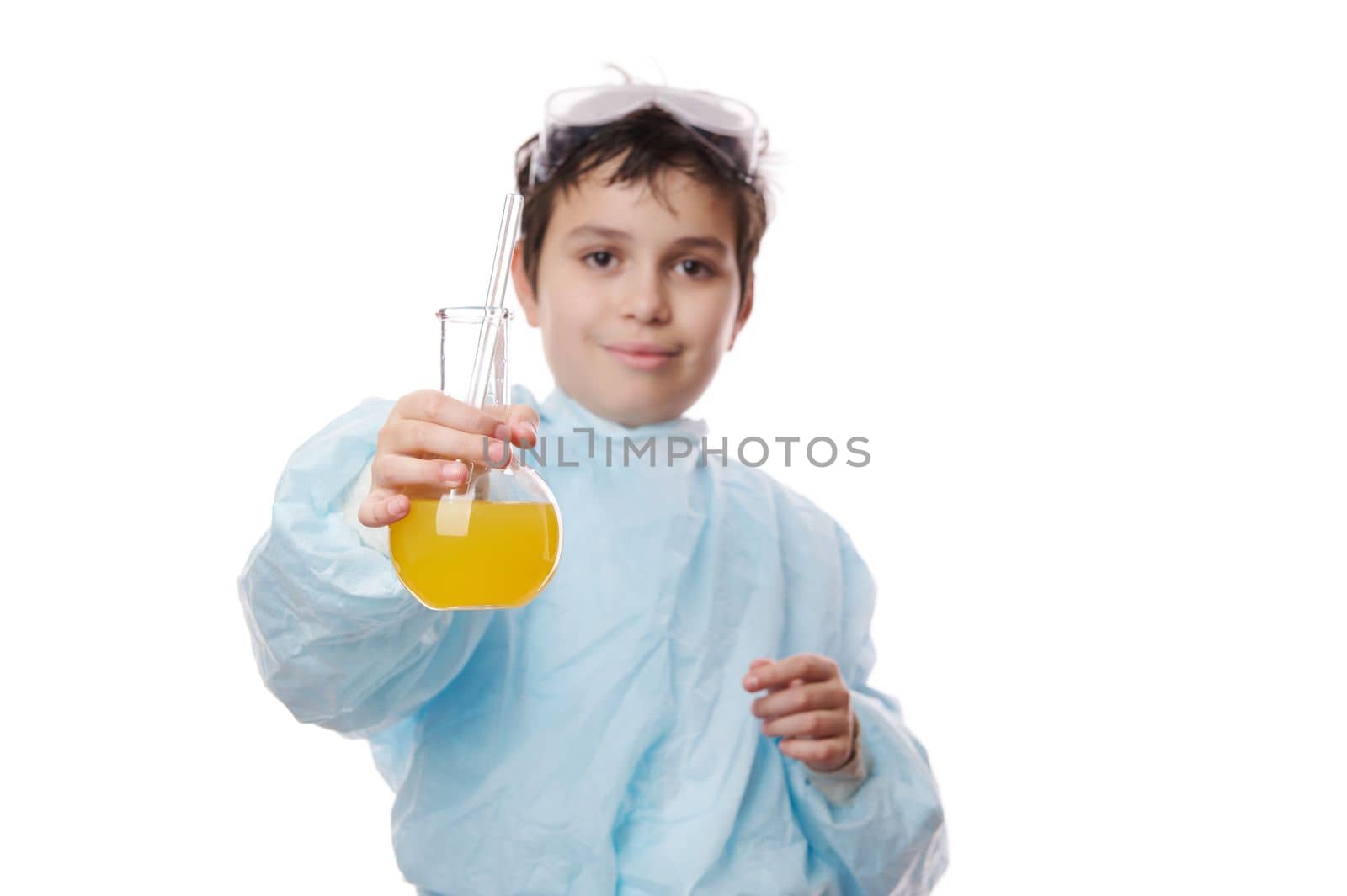 Focus on laboratory glass flask with yellow chemical solution, in the hands of a blurred smart teenage schoolboy, scientist chemist in lab coat, isolated over white background. Learning Chemistry