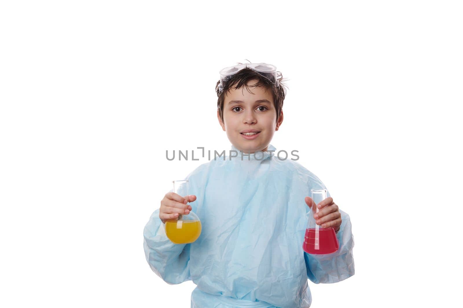 Adorable smart teenager schoolboy wearing lab coat, holding two laboratory glass flask with reagents and chemicals, conducting scientific experiments at chemistry class, isolated on white background