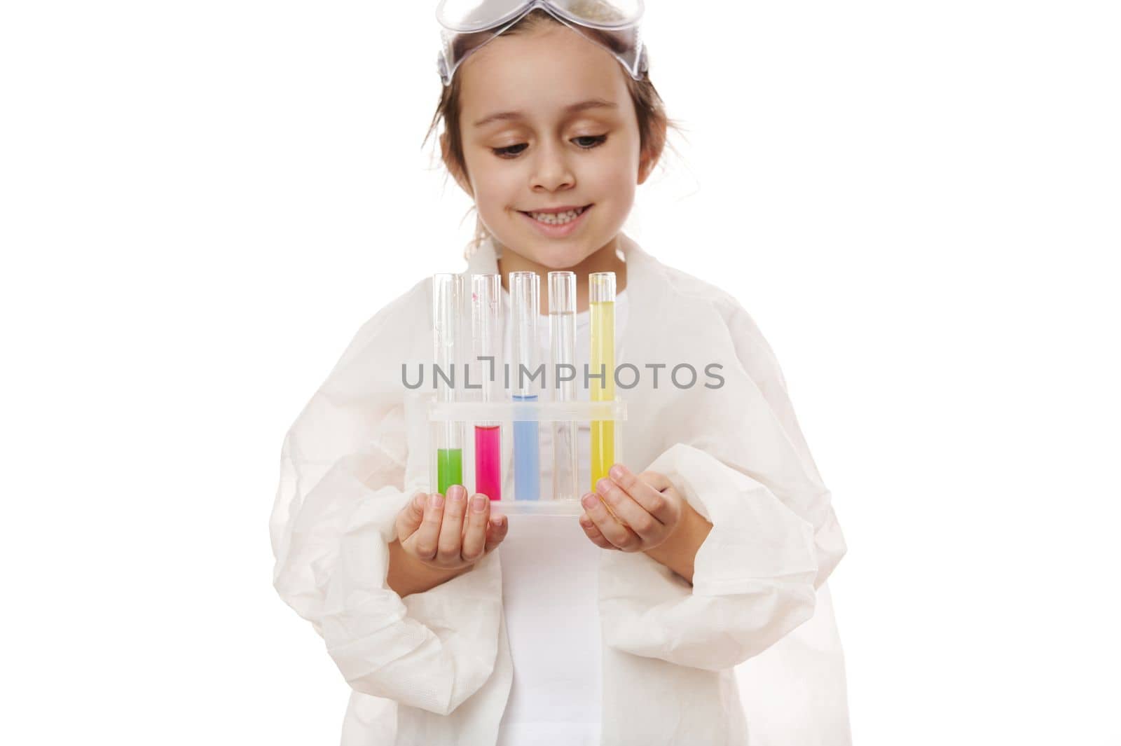 Selective focus on test tubes with colorful reagents and chemicals on tripod in the hands of a blurred child, little girl, young chemist scientist in lab coat, isolated on white background. Copy space
