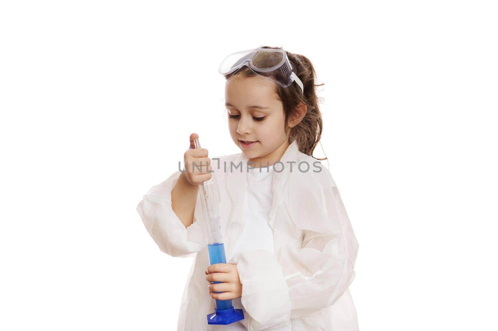 Smart little girl, student chemist-scientist in lab coat, dripping few drops of reagent from graduated pipette into a measuring cylinder with chemical solution, at a chemistry lesson. White background