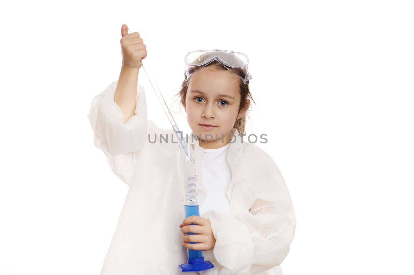 Smart preschooler child girl filling graduated pipette with blue substance from measuring cylinder, while conducting experiments in practical chemistry class, isolated over white background. Ad space