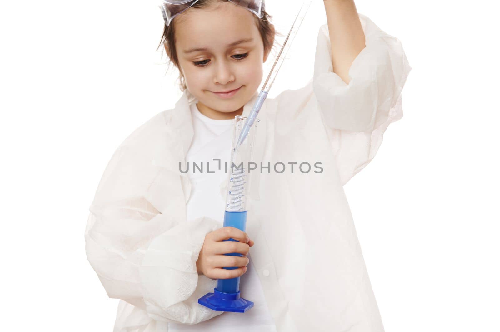 Close-up portrait of a little girl, young chemist scientist, filling the glass laboratory graduated pipette with a blue chemical solution from a measuring cylinder, isolated over white background