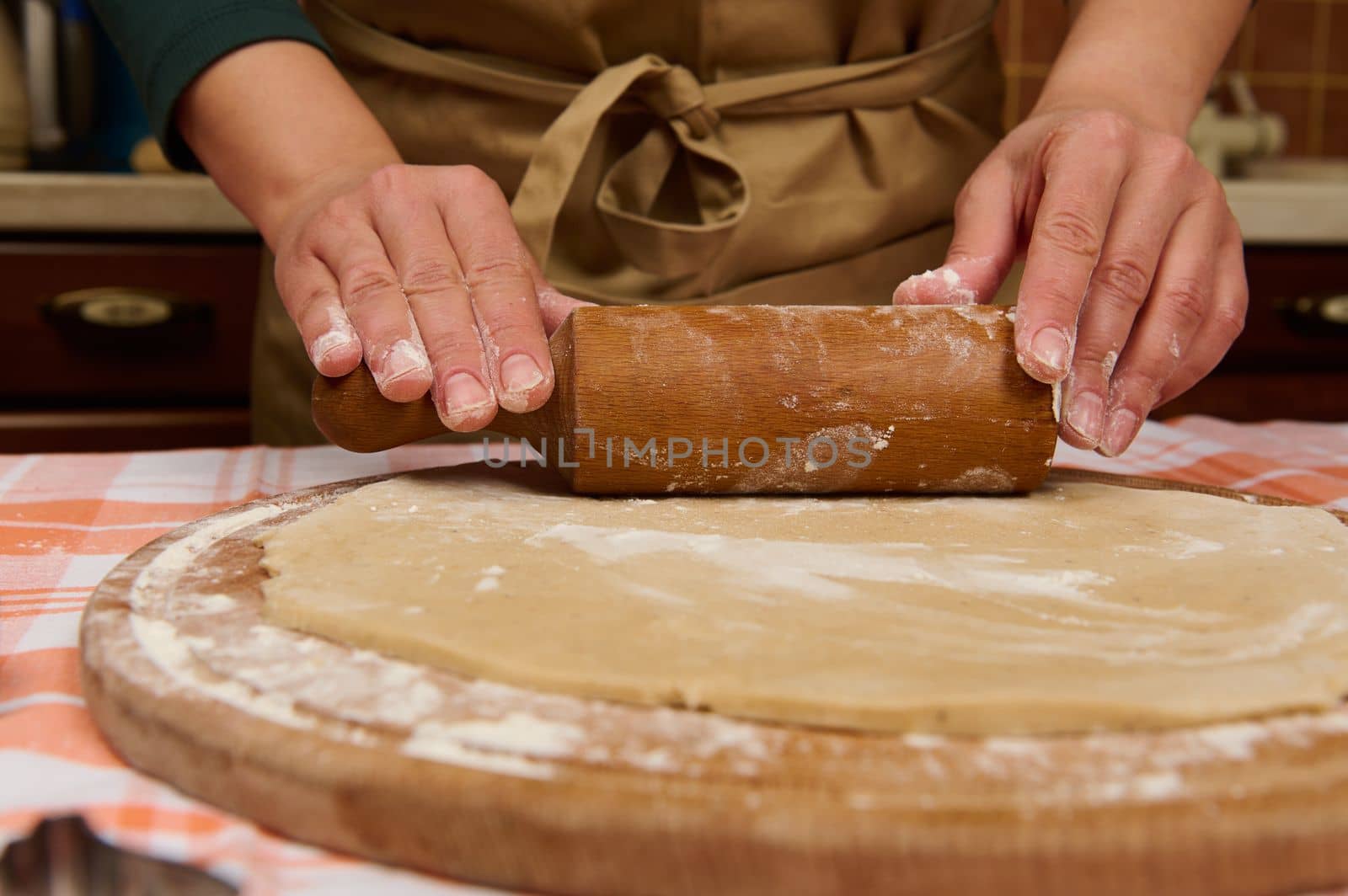 Details: Housewife, woman or chef confectioners hands using rolling pin, roll out the dough on a floured wooden board. Baking concept. Making pizza, bread, festive homemade pastries. Cookery. Culinary