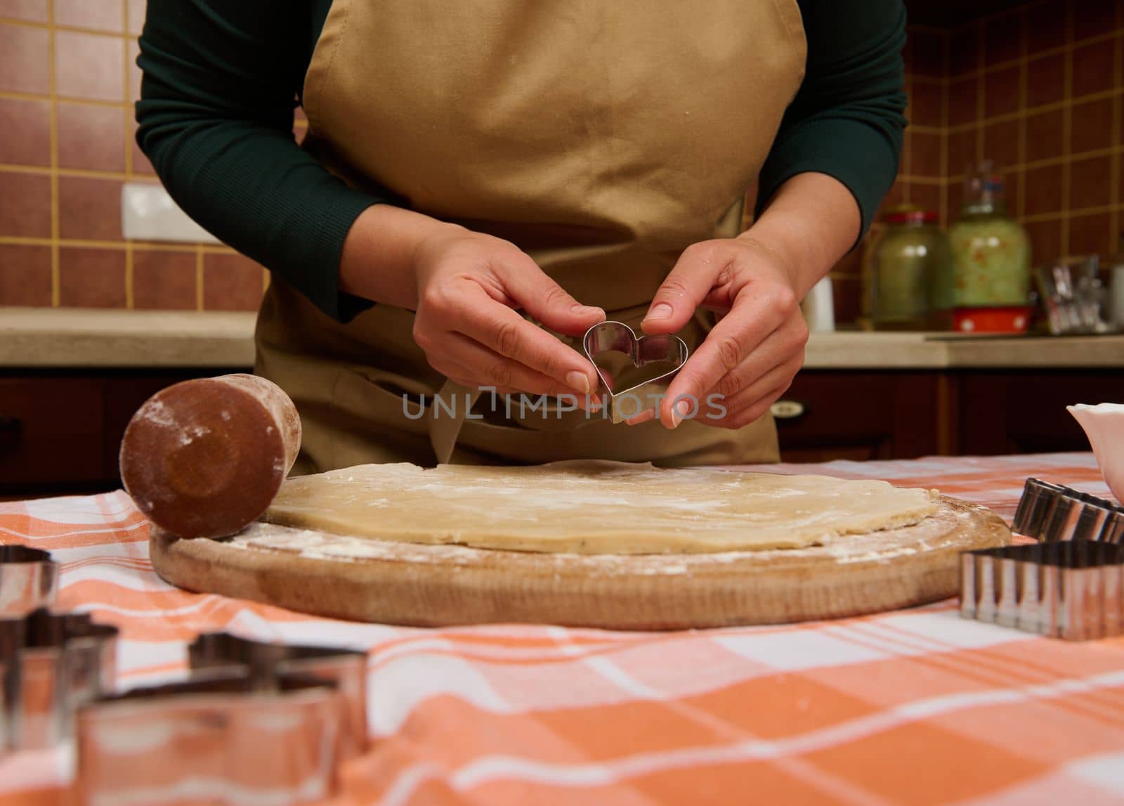 Details: hands of a woman chef confectioner, baker holding a heart shaped cookie cutter above a rolled out dough, while preparing gingerbread pastries for Christmas. Culinary. Baking festive items
