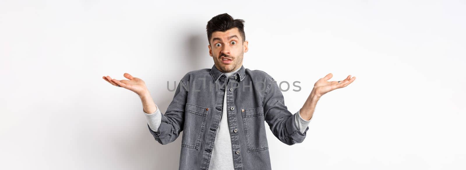 I dont know. Clueless young man shrugging and looking confused, have nothing to say, standing unaware on white background.