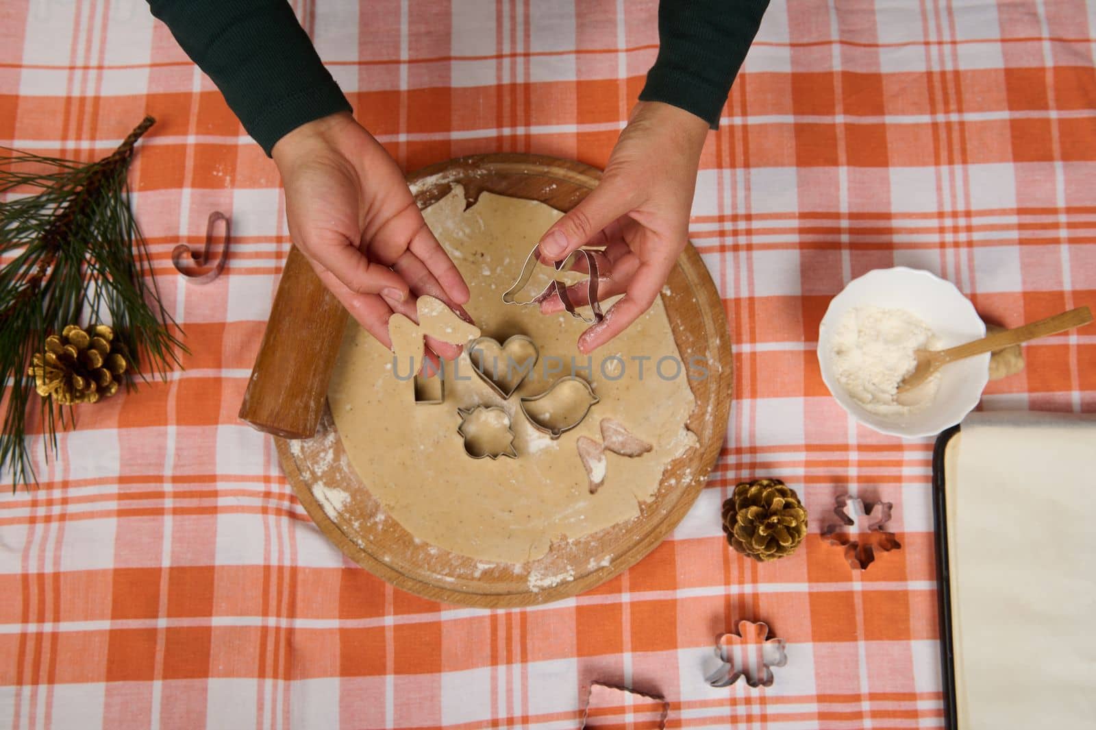 Christmas background with chef's hands cutting out shapes from gingerbread dough with cookie cutters. Close-up of a housewife confectioner preparing homemade cookies and pastries in the home kitchen