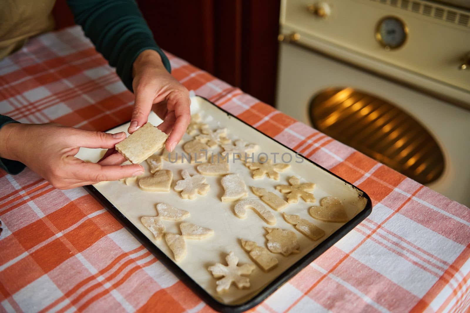 Close-up housewife putting cut out gingerbread cookies on the parchment, before baking in the hot oven. Christmastime by artgf