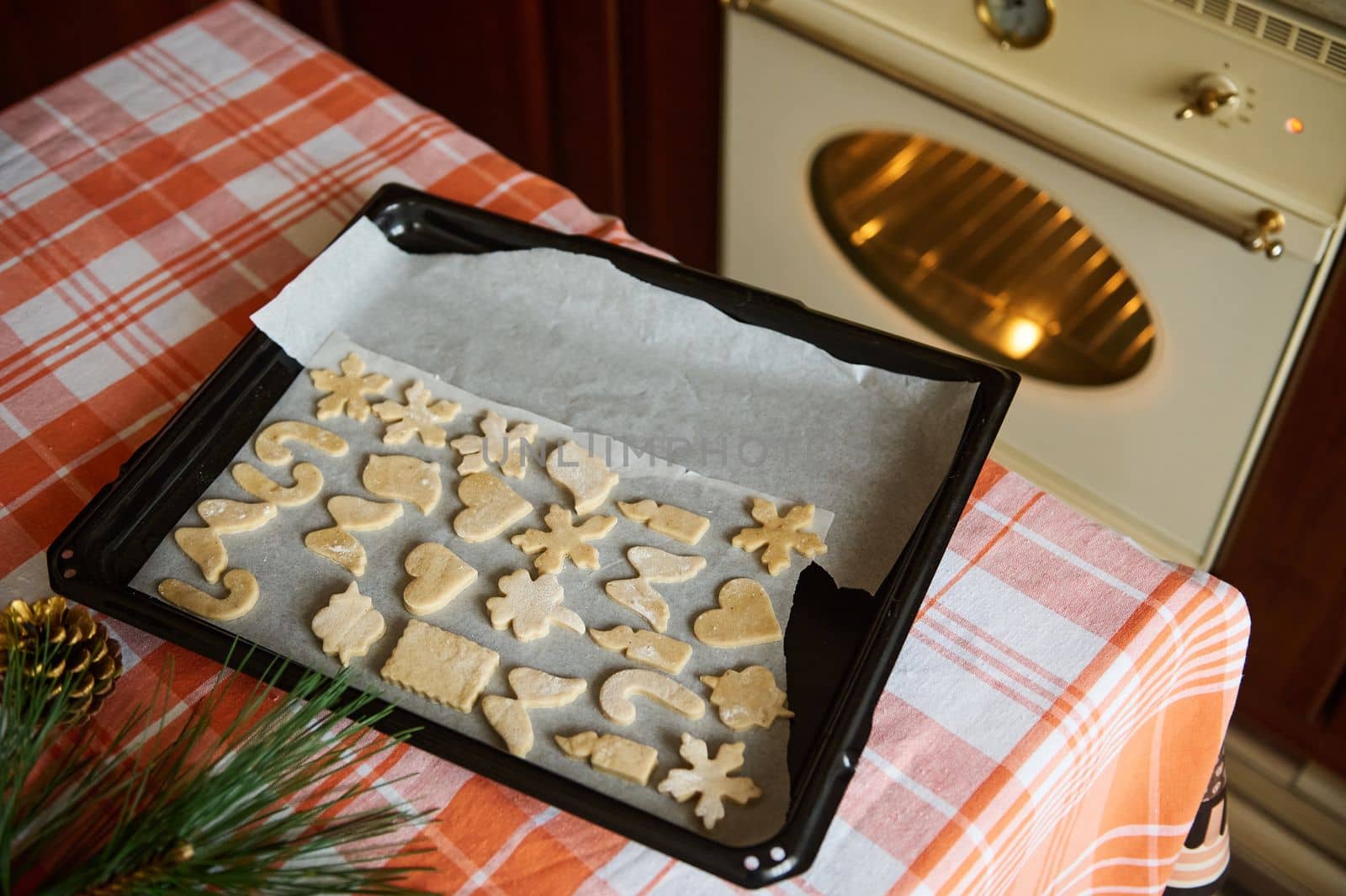 Top view baking sheet with cut-out gingerbread dough molds on the kitchen table against the backdrop of a heating oven by artgf