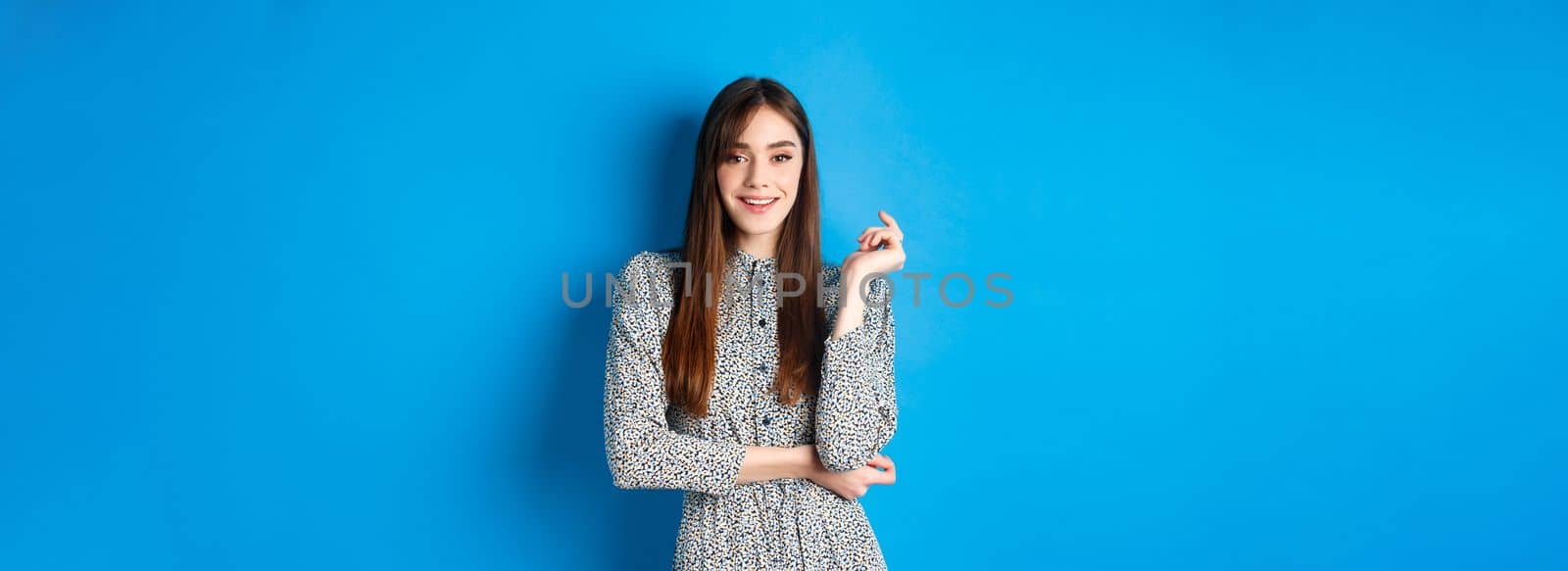 Beautiful caucasian woman 25s wearing dress, standing against blue background and smiling confident.