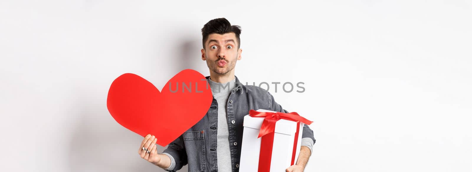 Valentines day and love concept. Guy waiting for kiss, bring lovely gifts and red heart card, pucker lips and look at camera, celebrating romantic holiday.