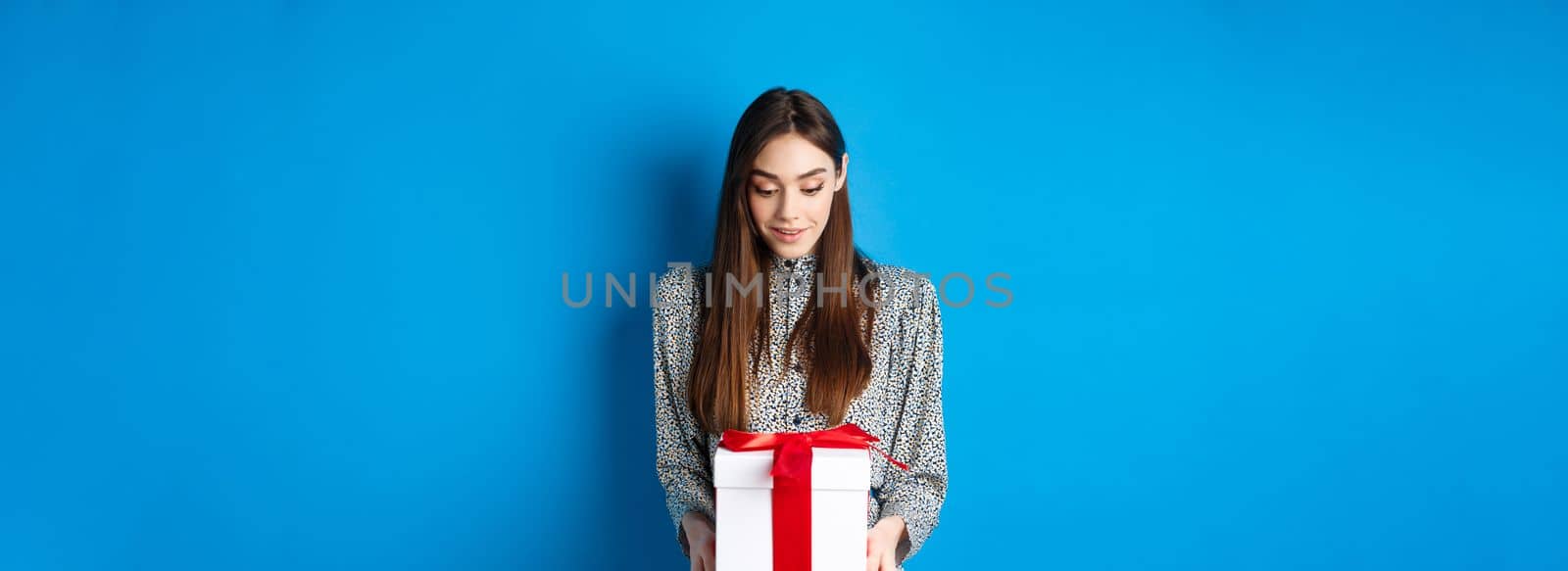 Valentines day. Surprised caucasian woman gasping amazed and looking at romantic gift, standing on blue background.