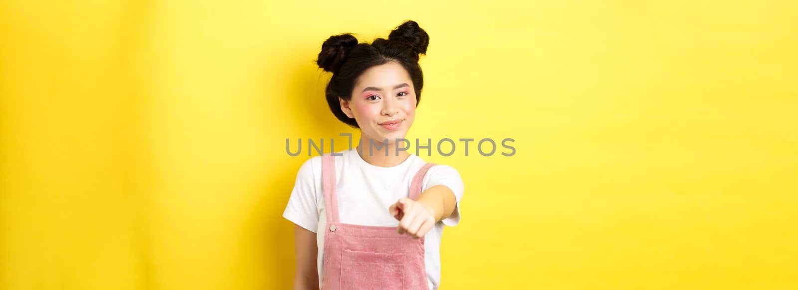 Stylish japanese girl with beauty makeup pointing at camera, smiling at you, beckon and invite people, standing on yellow background by Benzoix