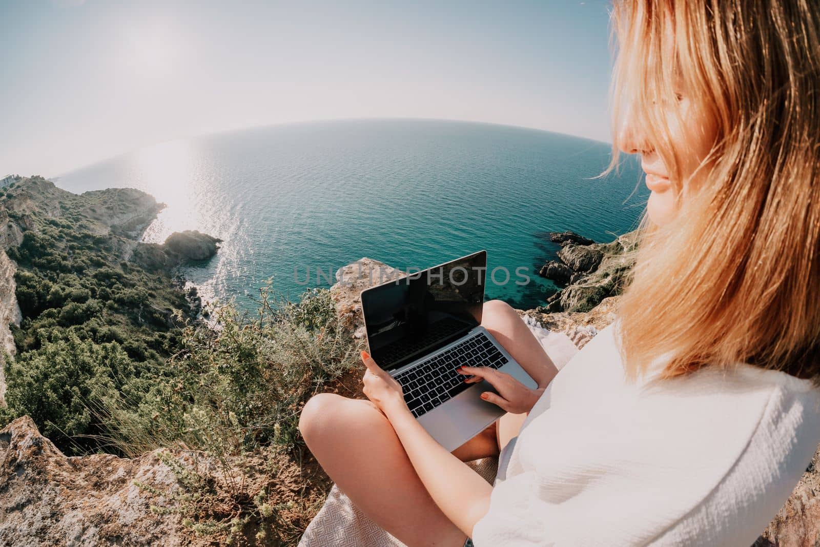 Woman sea laptop. Business woman in yellow hat working on laptop by sea. Close up on hands of pretty lady typing on computer outdoors summer day. Freelance, digital nomad, travel and holidays concept.