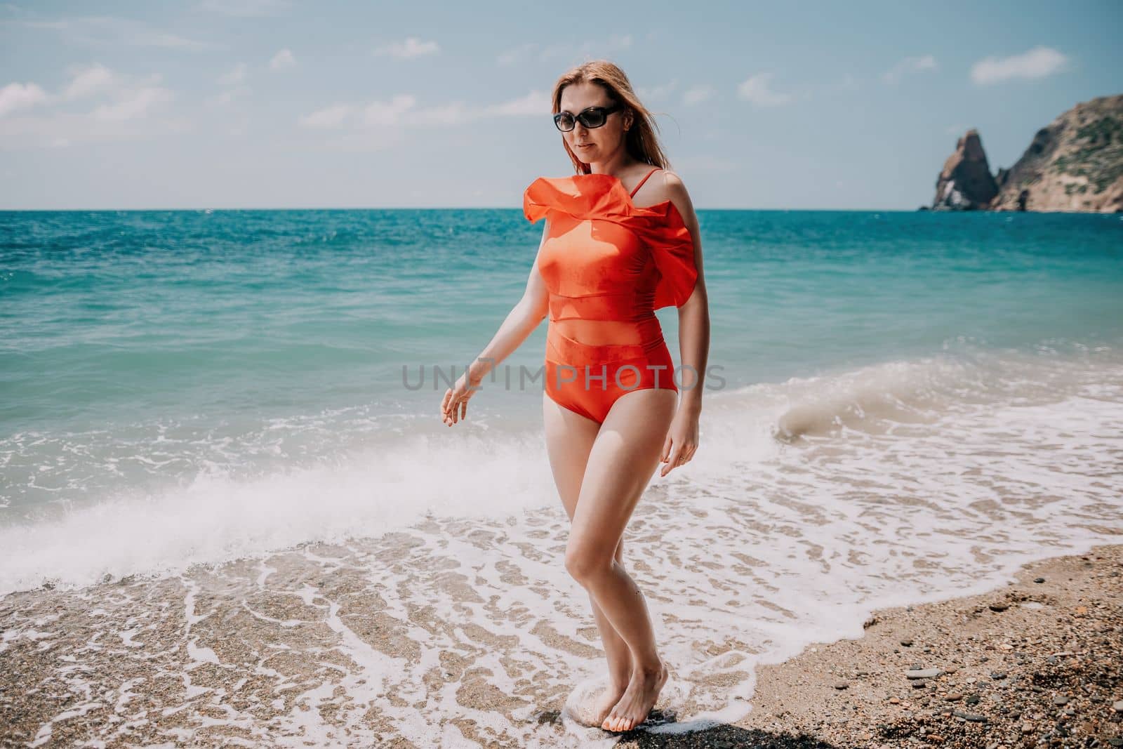 Young woman in red bikini on Beach. Blonde in sunglasses on pebble beach enjoying sun. Happy lady in one piece red swimsuit relaxing and sunbathing by turquoise sea ocean on hot summer day. Close up,