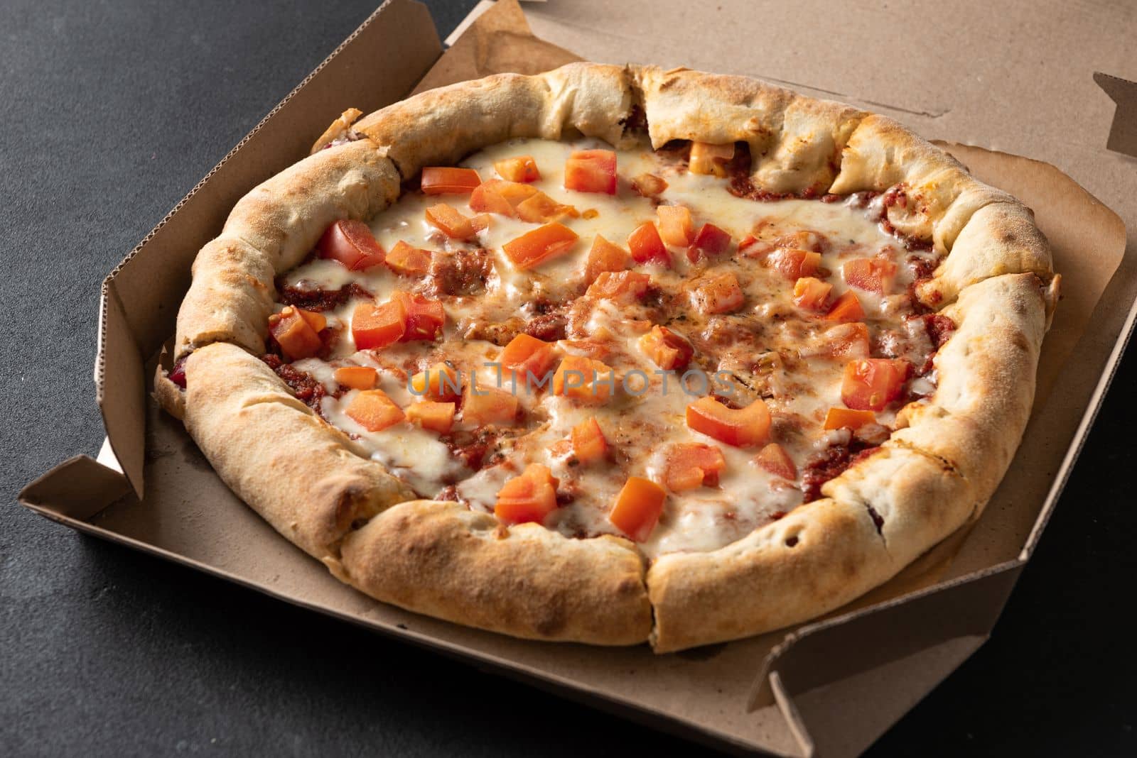 Pizza with tomatoes and mozzarella lies in a brown paper box. Pizza delivery.