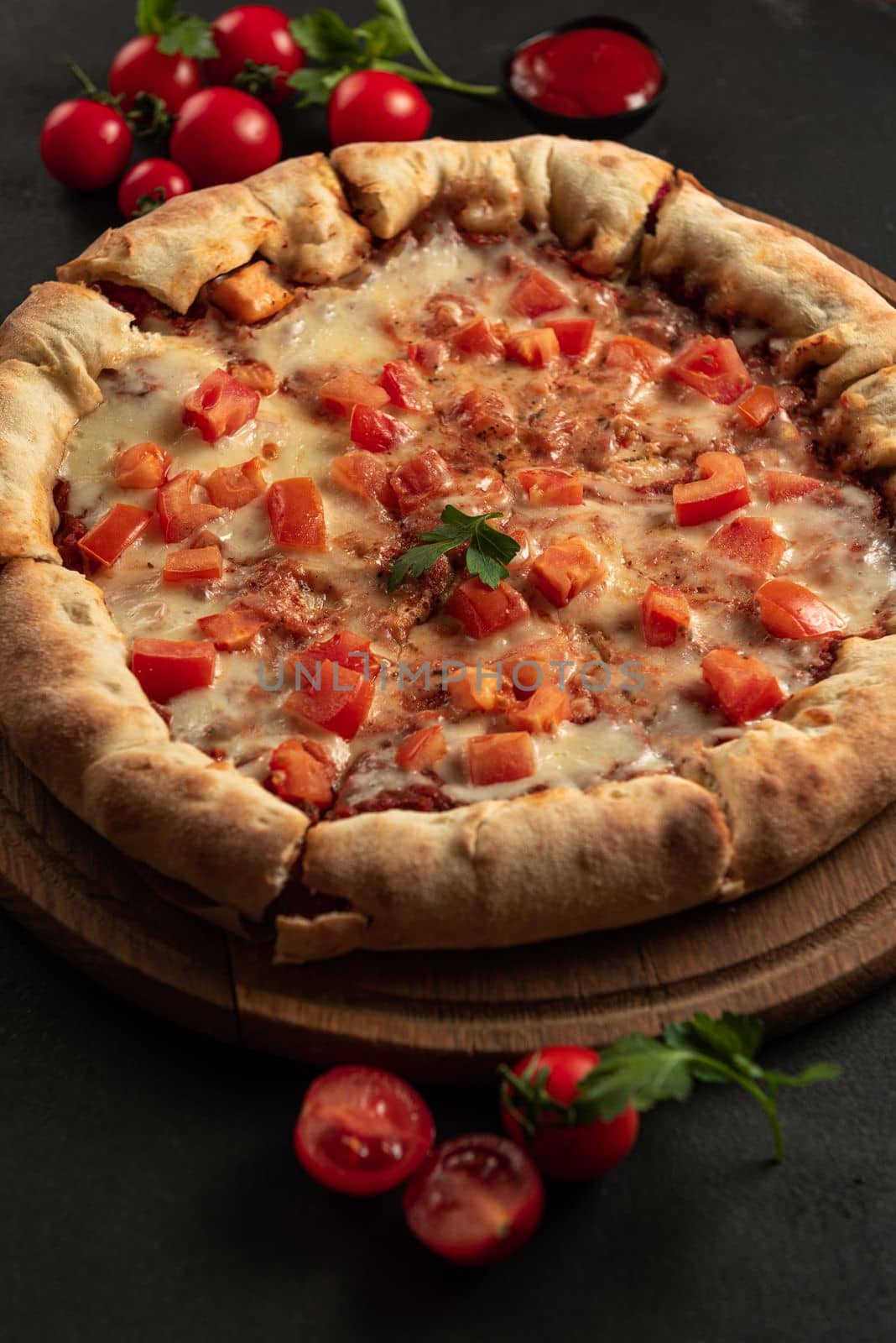 Vertical shot of a pizza with tomatoes on a dark background.