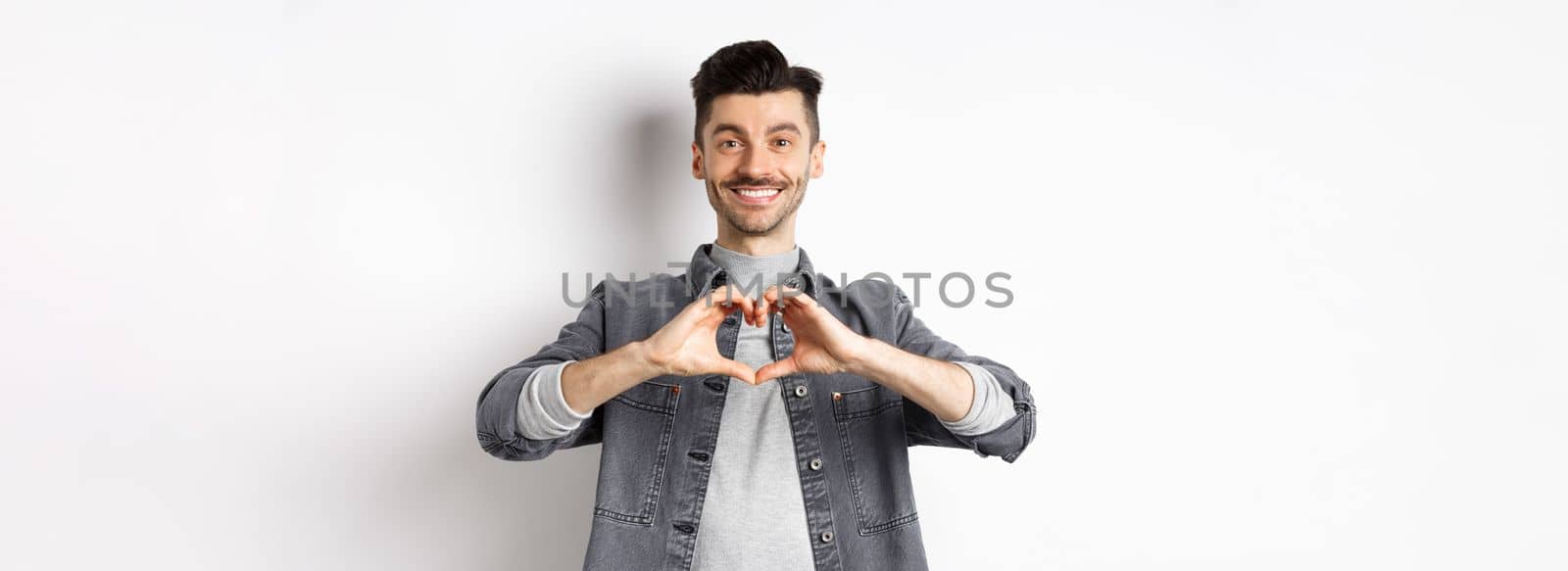 Handsome man showing heart gesture and smiling. Romantic guy say I love you and smiling tender at camera. Valentines day concept.