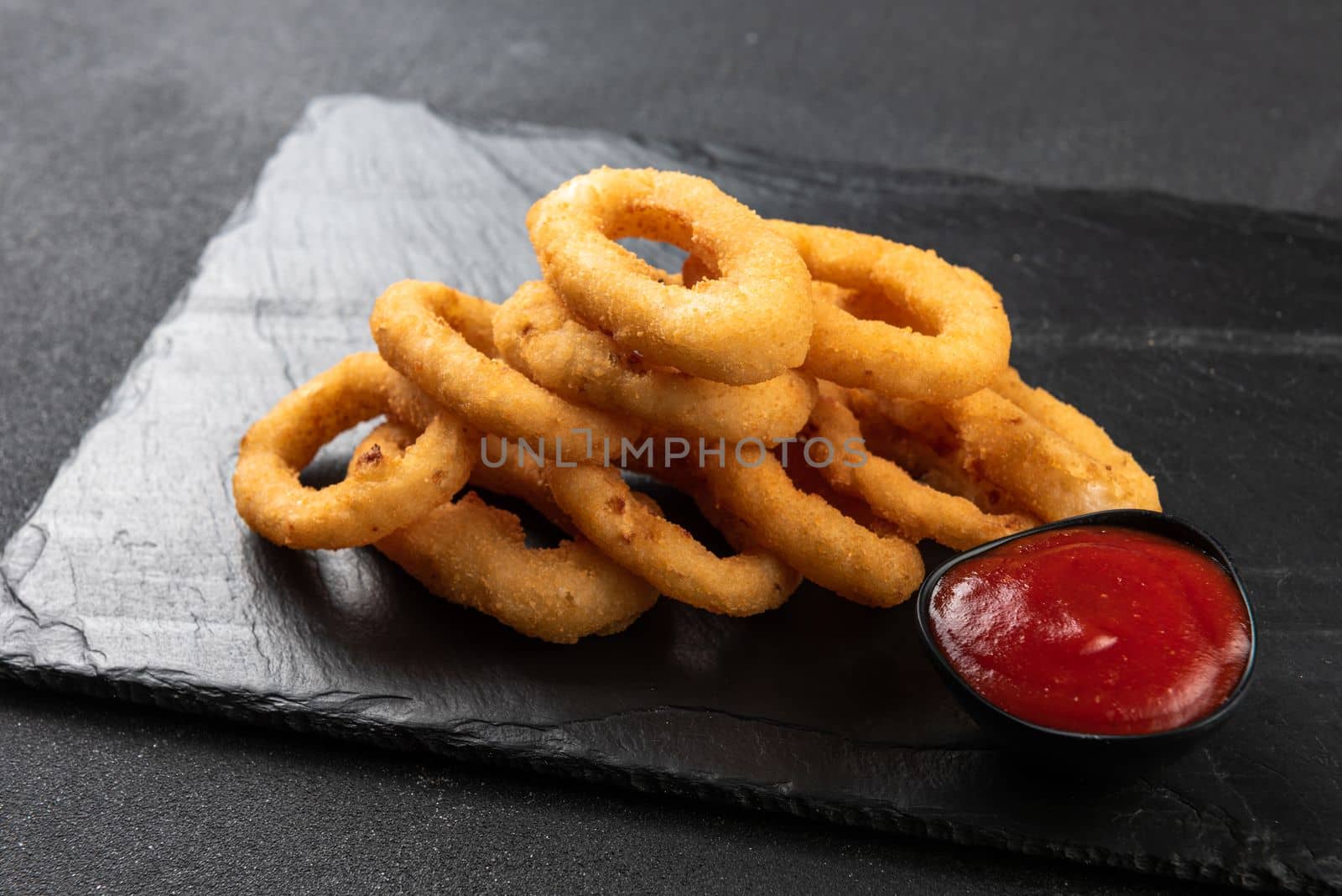 Calamari rings deep-fried in breading. Crispy squid rings on a dark background with sauce. by gulyaevstudio