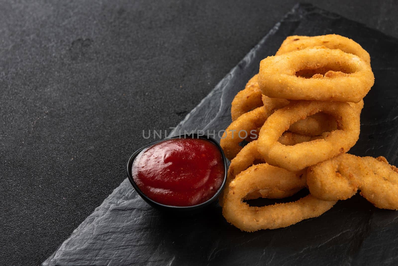 Calamari rings deep-fried in breading. Crispy squid rings on a dark background with sauce. Copy space