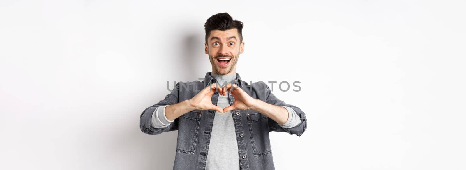 Romantic boyfriend showing heart gesture and looking with love at camera, celebrating White day after valentines, standing on white background. Romance concept by Benzoix