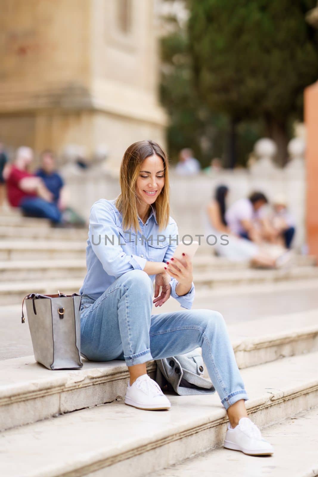 Glad woman with smartphone sitting on steps by javiindy