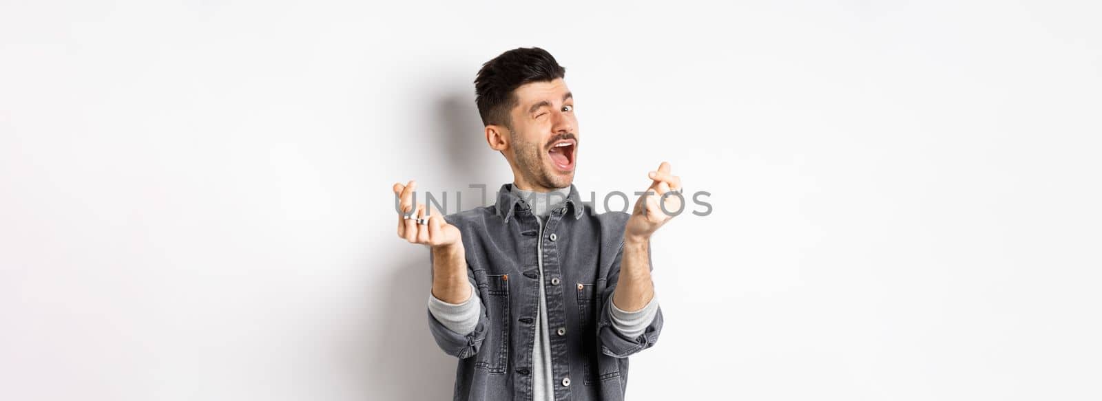 Funny guy winking and showing hand hearts sign, feeling romantic and happy, standing on white background.