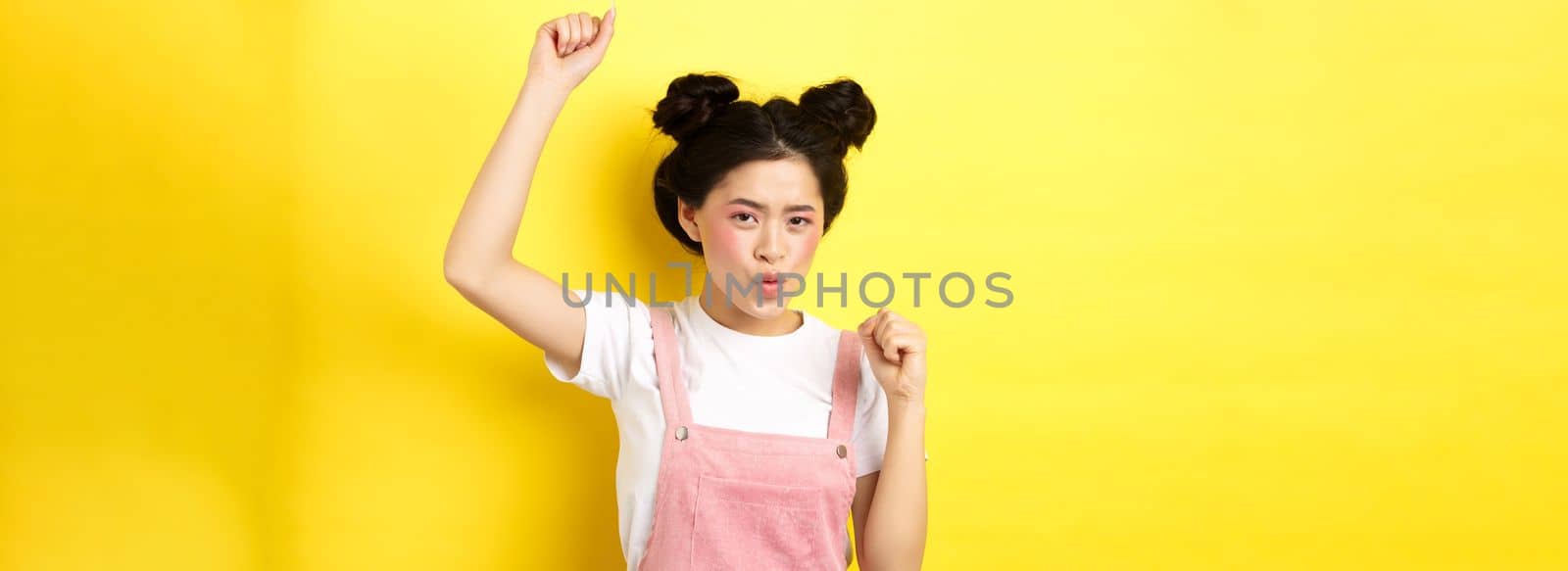 Excited asian woman getting motivation, raising hand up and chanting, celebrating victory, triumphing and standing on yellow background.