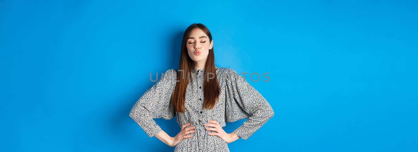 Valentines day and relationship concept. Romantic woman with closed eyes kissing lover, pucker lips and kissing you, standing on blue background by Benzoix