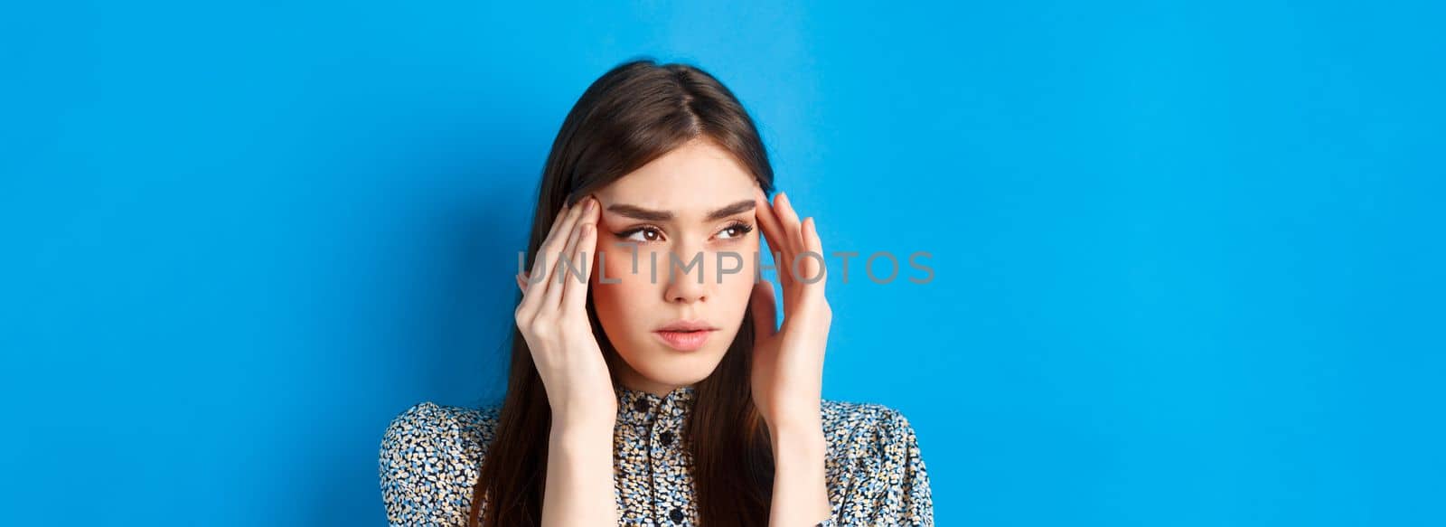 Close-up portrait of young woman feel sick, touching head temples and frowning from headache, having migraine, looking aside at logo, blue background by Benzoix