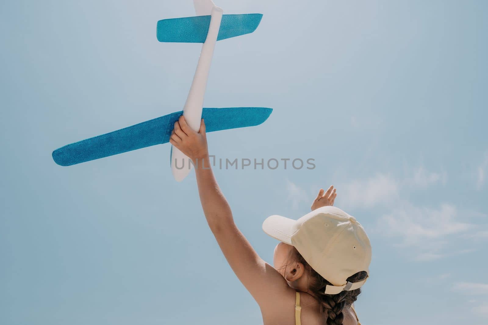 Kid playing with toy airplane. Children dream of travel by plane. Happy child girl has fun in summer vacation by sea and mountains. Outdoors activities at background of blue sky. Lifestyle moment