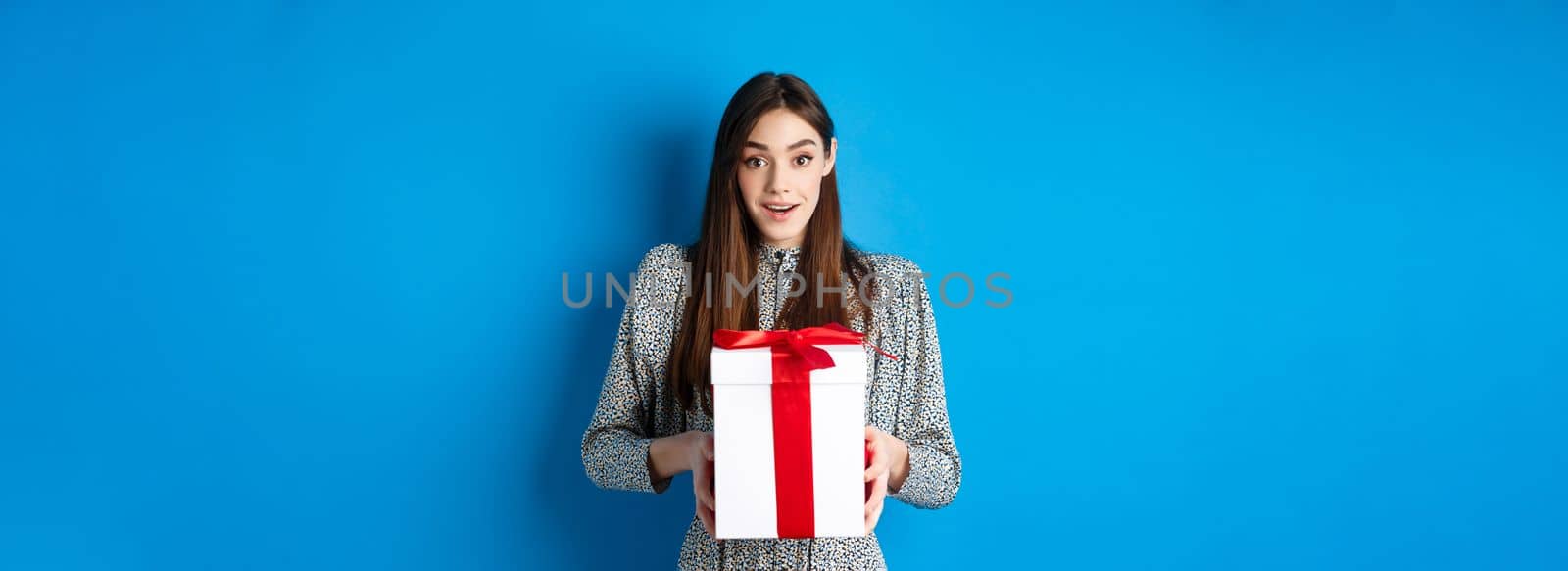 Valentines day concept. Surprised happy girl receiving romantic gift and looking thankful at camera, standing on blue background.