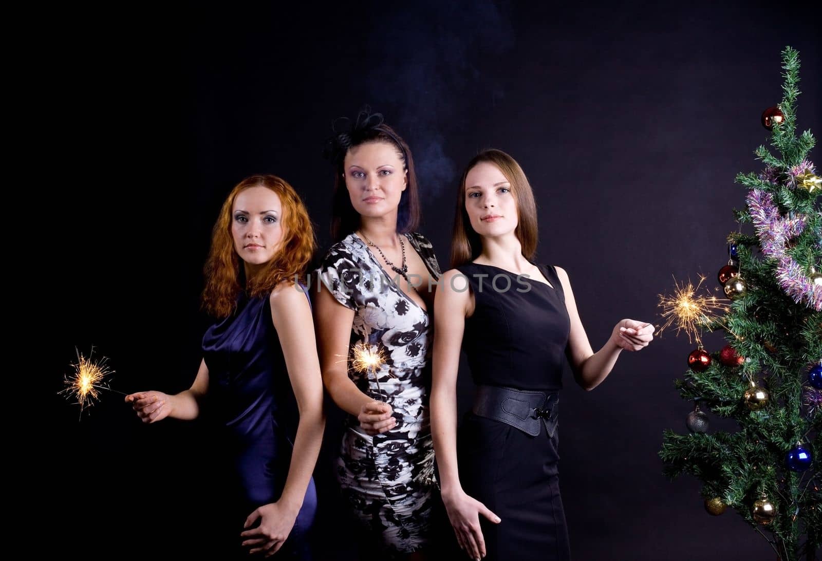 Three girls and christmas tree with bengal light