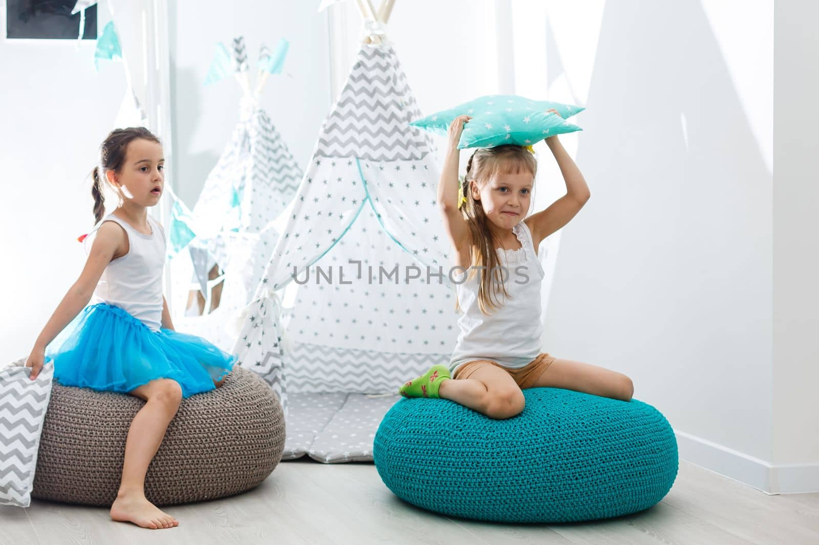 Stay Home Stay Safe. Two happy kids sitting on cozy chair relaxing playing in white living room indoors. Sisters having fun at home by Andelov13