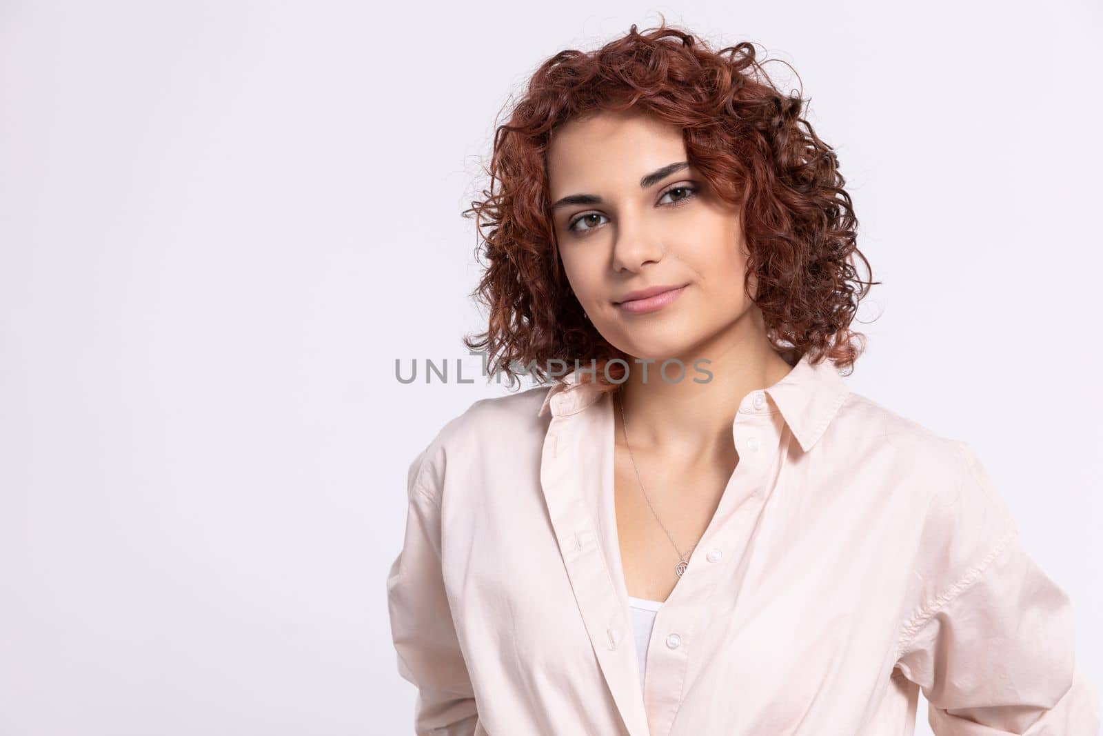 A gentle smile on her face. A European woman with chestnut-colored hair. A girl with fair skin and curly short hair looks straight ahead.