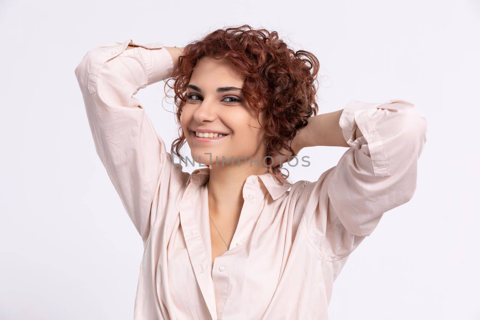 Smiling and full of sincere joy, the girl raises her hair up with her hands. Beautiful short curly chestnut-colored hair. Natural hairstyle.
