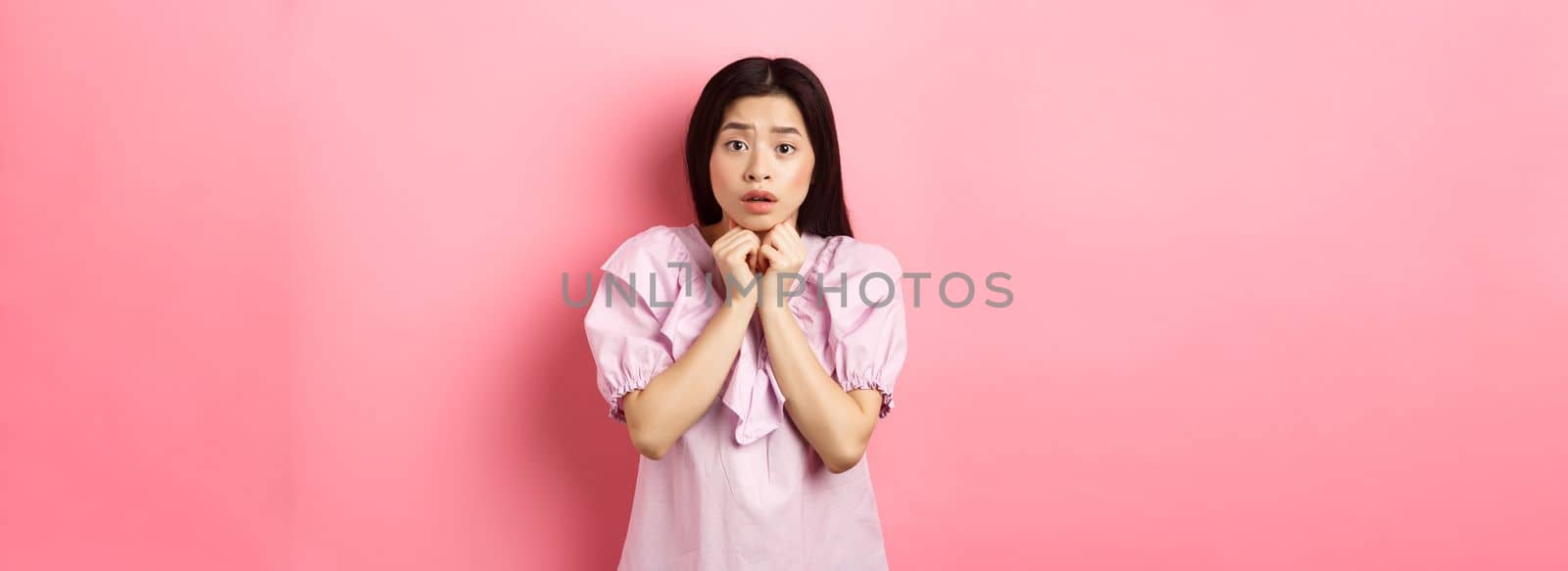 Scared timid girl looking worried at camera, standing concerned on pink background by Benzoix